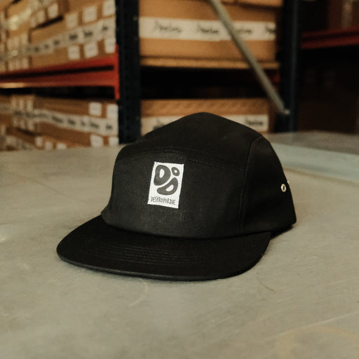 Black cap with a logo on a concrete floor with stacked boxes in the background