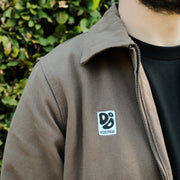 Brown jacket with a logo patch on the chest against a blurred green background