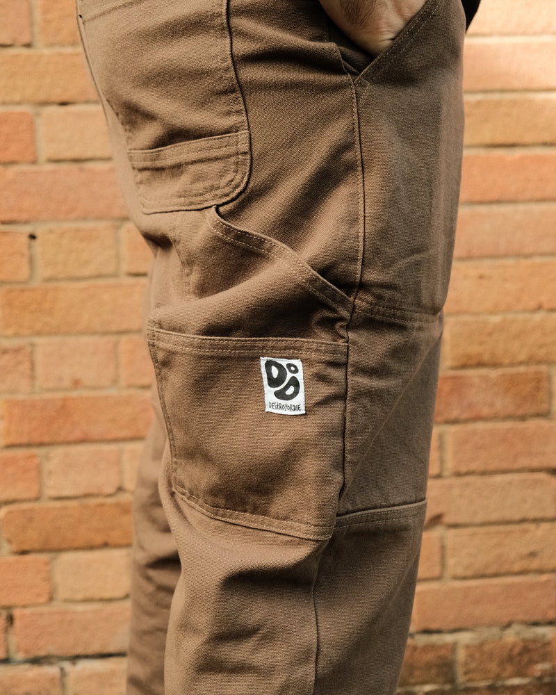 Brown pants with a logo on the pocket against a brick wall