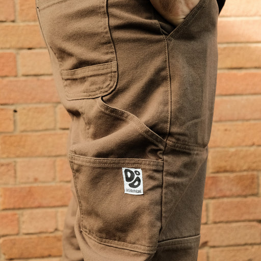 Brown pants with a logo on the pocket against a brick wall