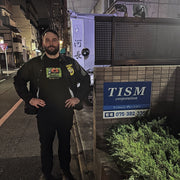 Man standing on a street at night in front of a building with a 'TISM corporation' sign.